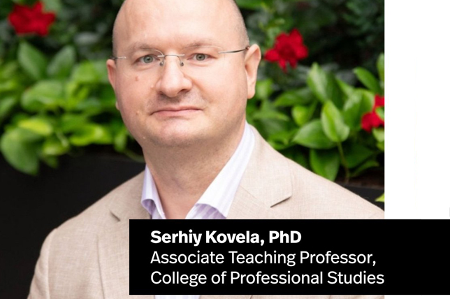 Dr. Serhiy Kovela, Associate Teaching Professor at Northeastern University's College of Professional Studies wears a tan jacket. Verdant foliage and red flowers are behind him.