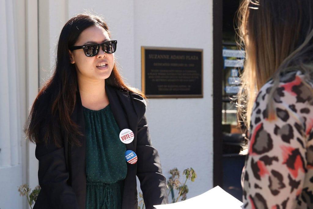 Student wearing sunglasses and voter buttons talks with another student on Suzanne Adams Plaza on Northeastern University's Oakland campus